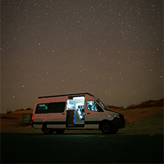 White camper van glowing from interior lighting under a starry sky in a remote beach