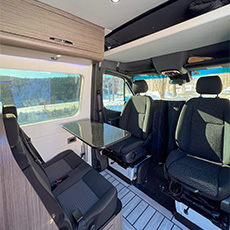 Driver and passenger captain’s chairs facing a dinette table in compact van layout