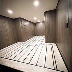 Interior camper van cargo area with wood-look flooring and curved cabinetry under ceiling lights